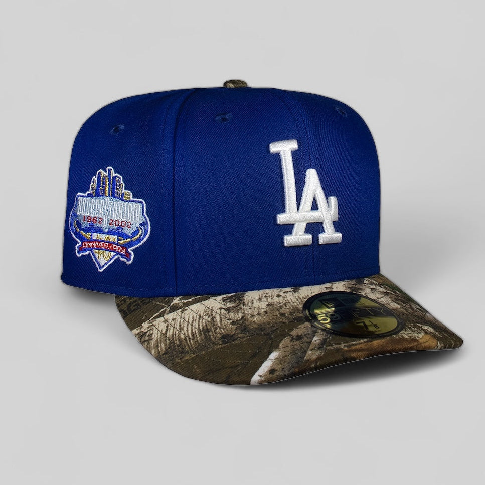 A fitted baseball cap with the Los Angeles Dodgers logo in white on a blue crown, featuring a camouflage pattern on the visor, and an emblem on the side.